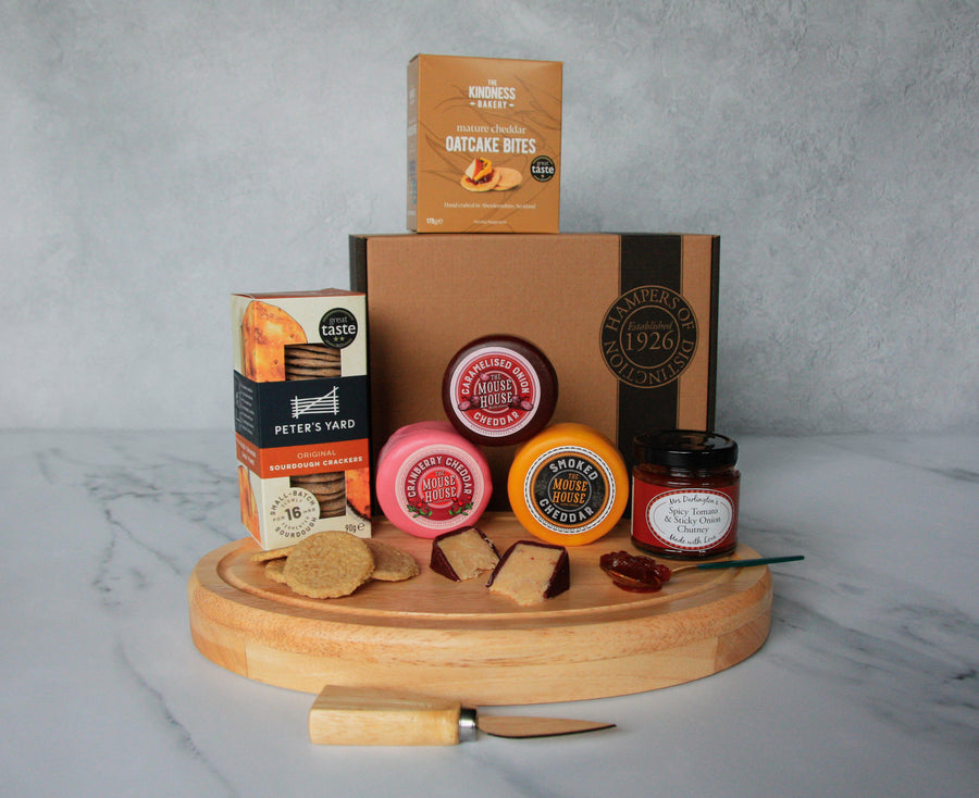 The Three Cheese Hamper laid out on a table top and a cheeseboard. Including Mouse House cheeses and other savoury snacks in this gift.